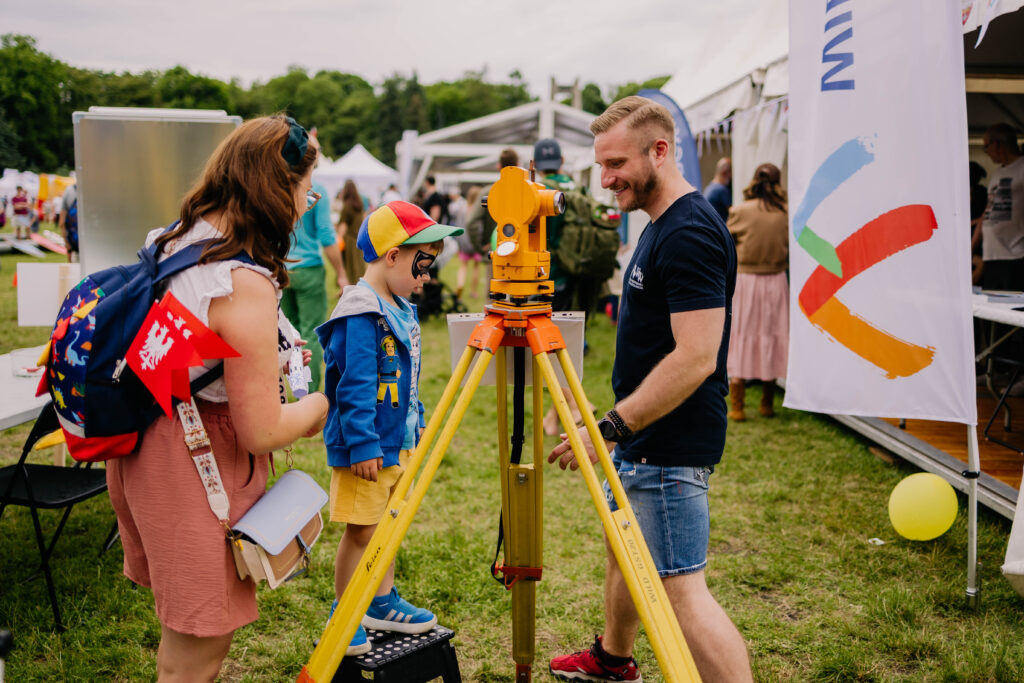 Trzy osoby obok geodezyjnego sprzętu pomiarowego